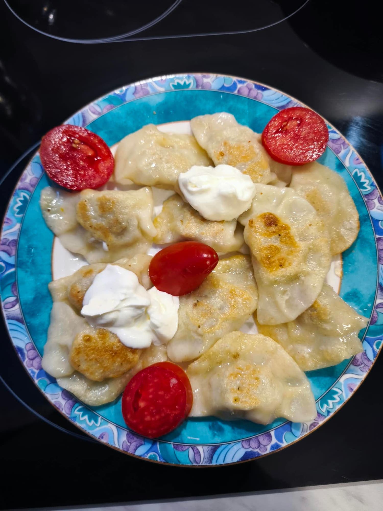 Pierogi ruskie polane śmietaną, na talerzu z pomidorami