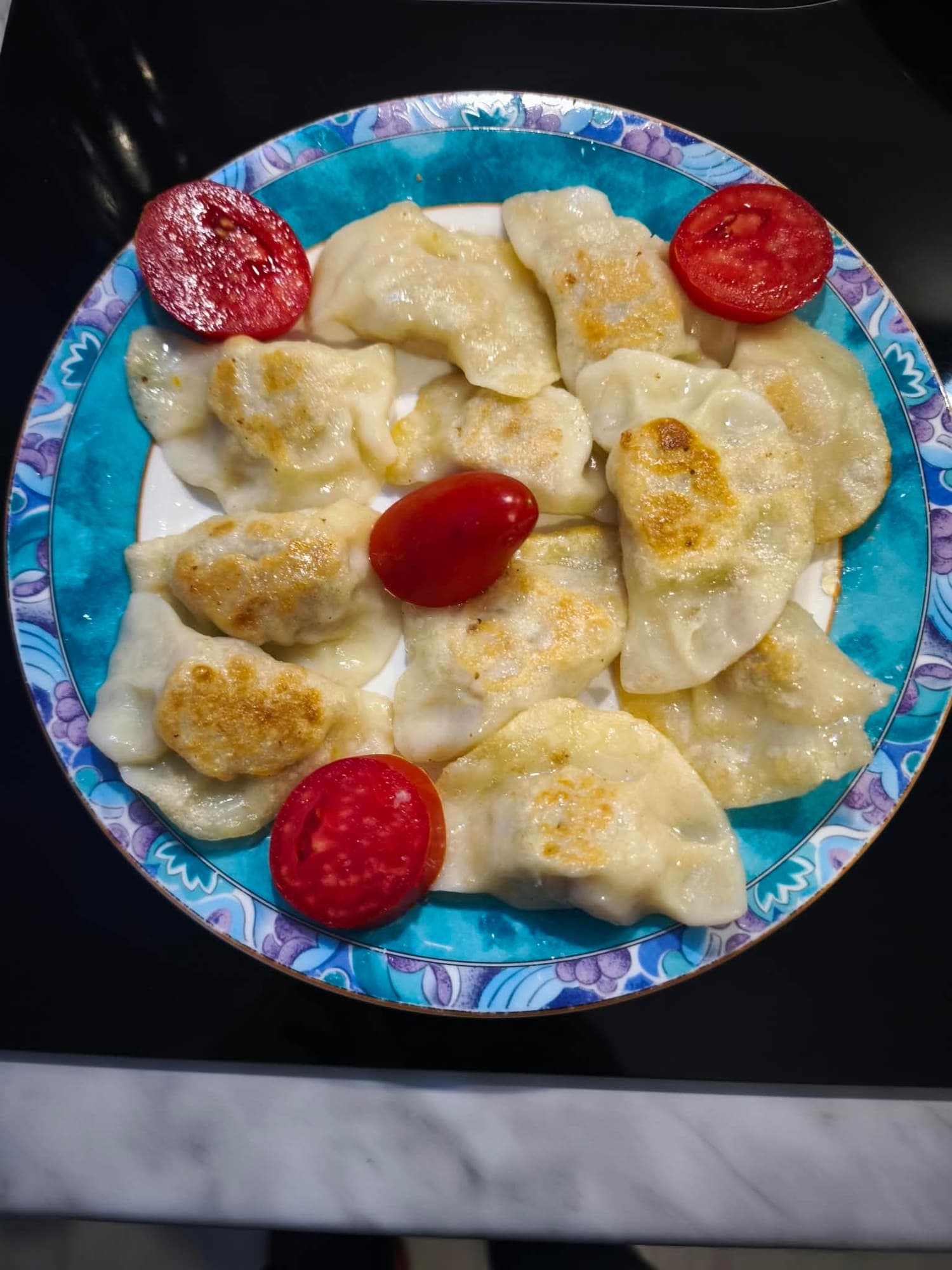 Pierogi ruskie polane śmietaną, na talerzu z pomidorami